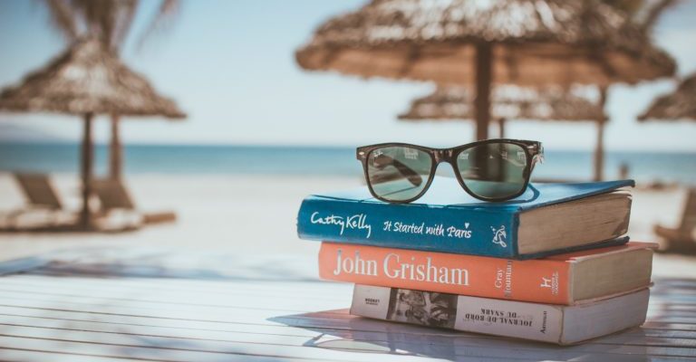 Sunglasses resting on a stack of books with a tropical beach in the background