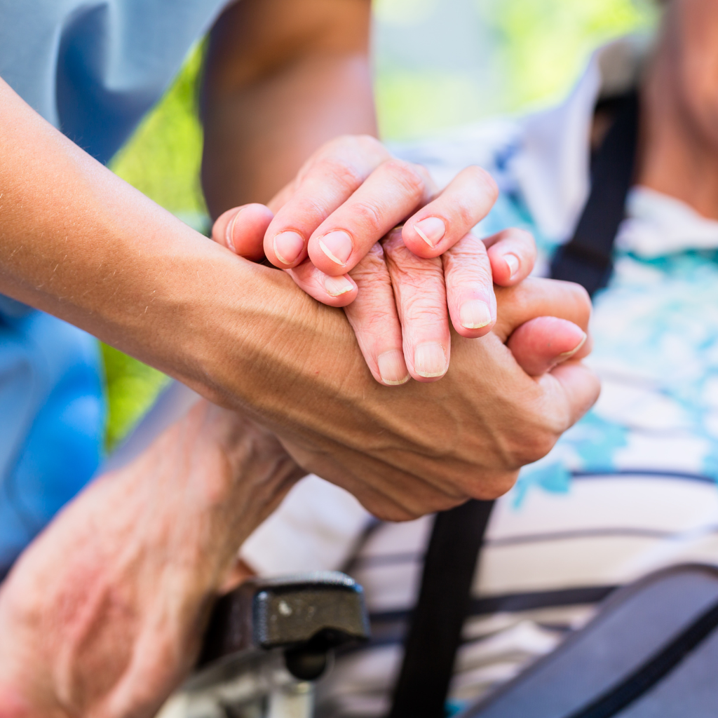 Close-up of a caregiver's hand gently holding the hands of an elderly person in a wheelchair, symbolizing aging well and support.